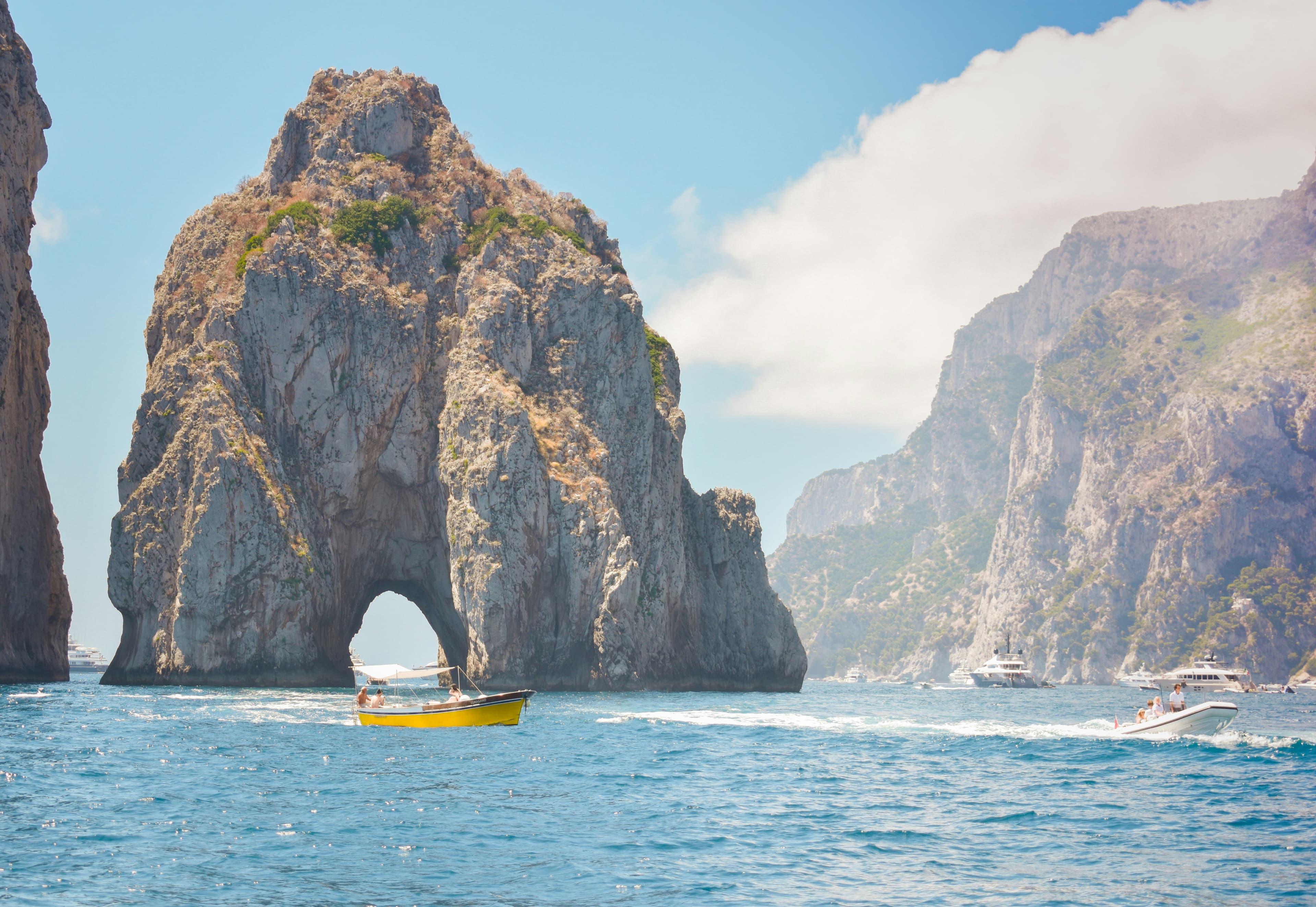Yellow gozzo boat passing through the Faraglioni arch in Capri